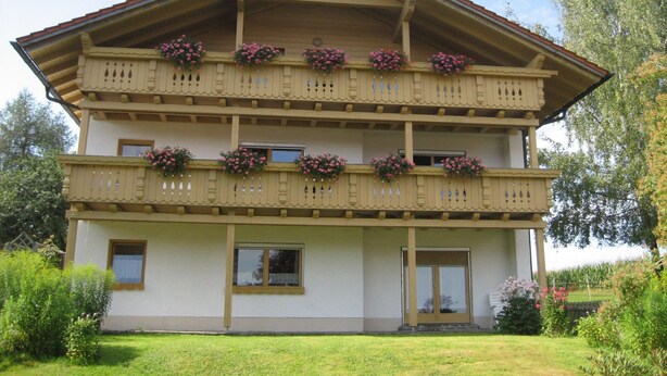 Un edificio de dos pisos con balcones decorados con jardineras, techo plano y entrada principal.