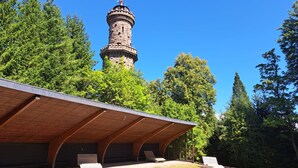 A modern building with a wooden roof and a stone tower in the background. - Apartment Bär by Interhome (Baiersbronn)