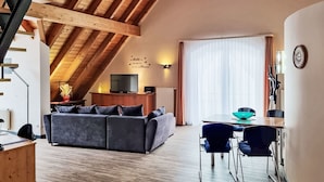 A loft-style living area with a high ceiling, wooden beams, a sofa, a dining table with chairs, a television, and a clock on the wall. - Apartment Bär by Interhome (Baiersbronn)