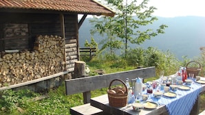 A rustic wooden cabin with a table set for a meal, surrounded by greenery and a mountainous backdrop. - Tauchert by Interhome (Baiersbronn)