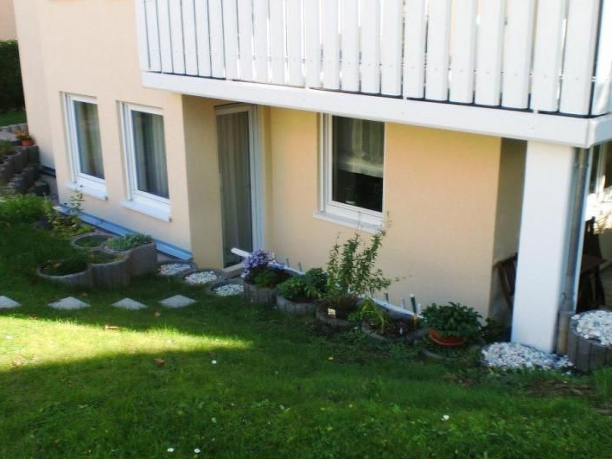 Ein zweistöckiges Gebäude mit einem Balkon, einem kleinen Garten mit trittsteinförmigen Wegen und einem Pfad zum Eingang.