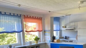 Ein gemütlicher Wohnbereich mit Sofa, Sessel und kleinem Holztisch. Eine Küchenzeile ist erkennbar, mit Herd, Spüle und Schränken.