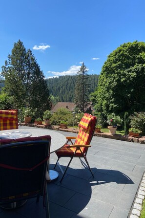 An outdoor patio with a round table and two chairs, surrounded by potted plants and a view of a forested area. - Apartment  by Interhome (Freudenstadt)