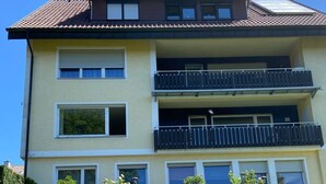 Ein mehrstöckiges Gebäude mit Balkonen, einer flachen Dachterrasse und einer Steinmauern mit Blumentöpfen.