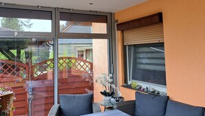 A sunlit room with a large sliding glass door leading to a patio, a cushioned seating area, and a small table with decorative items. - Waldperle by Interhome (Altwarp)