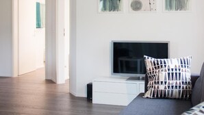 Een moderne woonkamer met een flatscreen televisie, een bank en een salontafel. Boven de televisie hangen drie schilderijen.