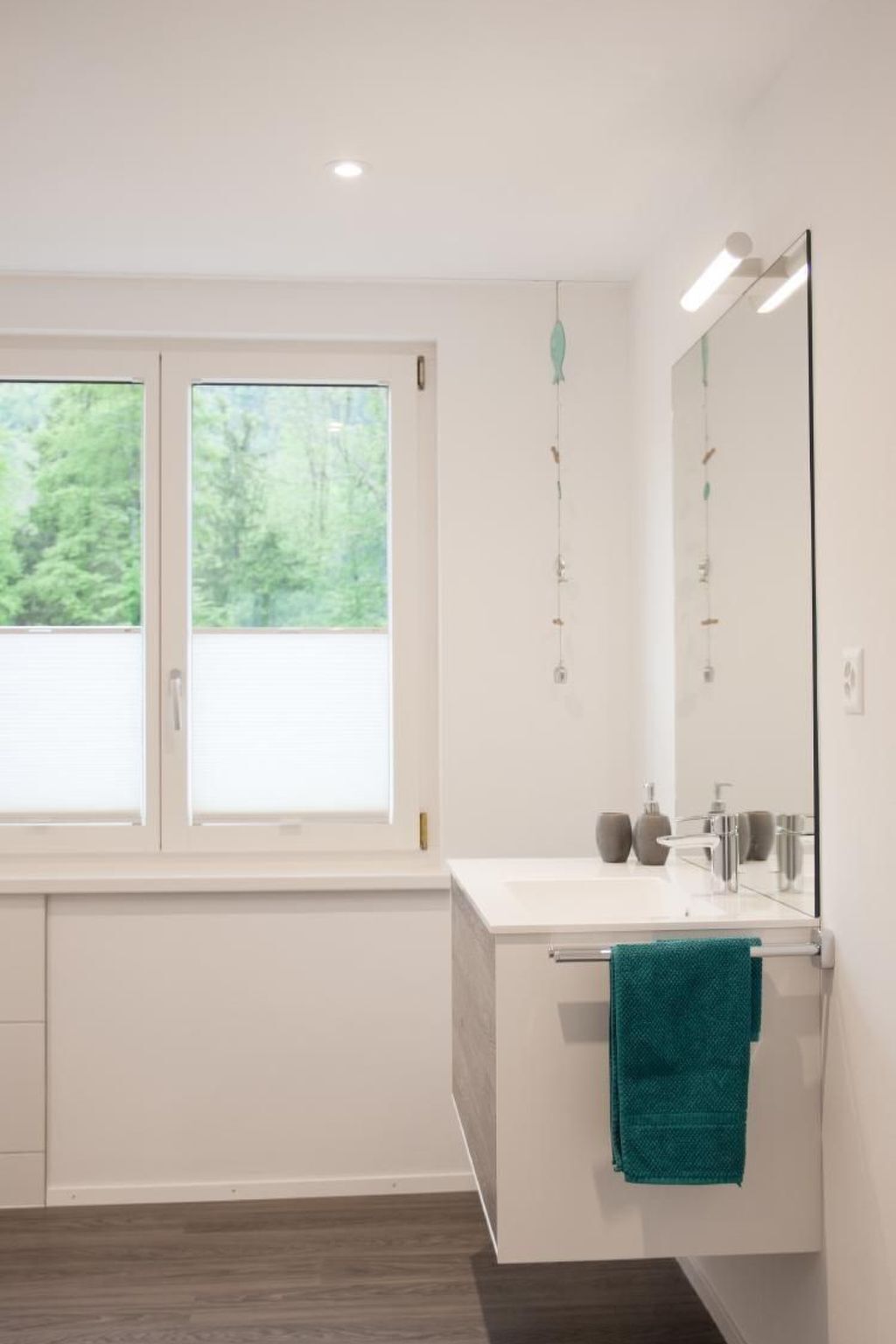 Ein modernes Badezimmer mit einem großen Fenster, einem weißen Waschtisch, einem Spiegel und einem türkisfarbenen Handtuch.