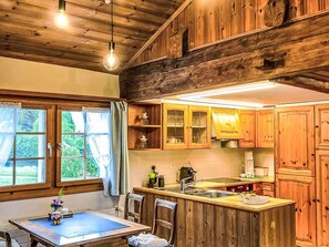 A rustic kitchen with wooden cabinets, a central island with a sink, and a dining area with a table and chairs. - Scheftenau by Interhome (Wattwil)
