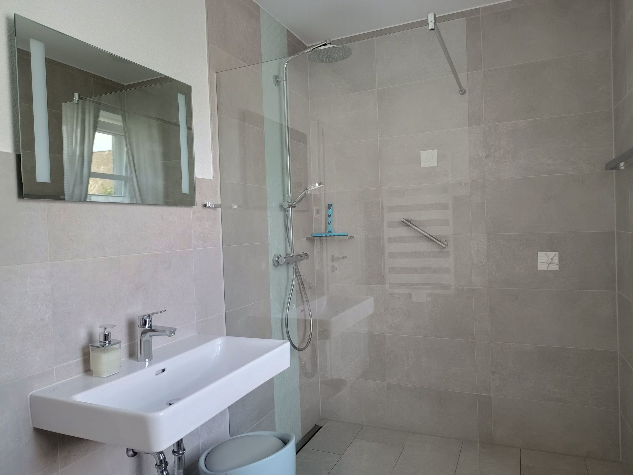 A modern bathroom with a glass-enclosed shower, a white sink, and a mirror above it.