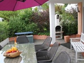 Una veranda esterna con mobili in vimini, un tavolo con della frutta e un forno per la pizza.