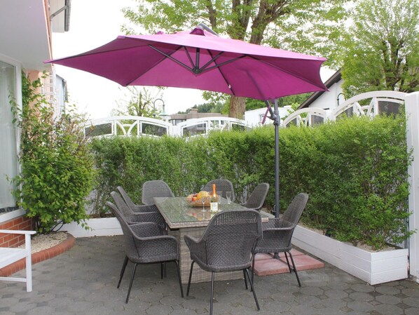 An outdoor patio with a table and chairs, a purple umbrella, and a white fence.