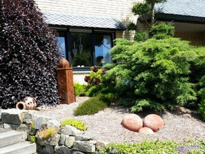 A well-maintained garden with a variety of plants, a decorative metal fence, and a stone pathway leading to a building with large windows. - Himmelreich by Interhome (Bruchhausen)