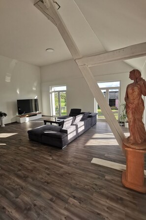 Ein geräumiges Wohnzimmer mit einer großen, schwarzen Eckcouch, einem Flachbildfernseher und Holzböden.