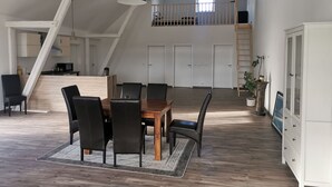 A spacious dining area with a wooden table and chairs, a hanging light fixture, and a staircase leading to an upper level.