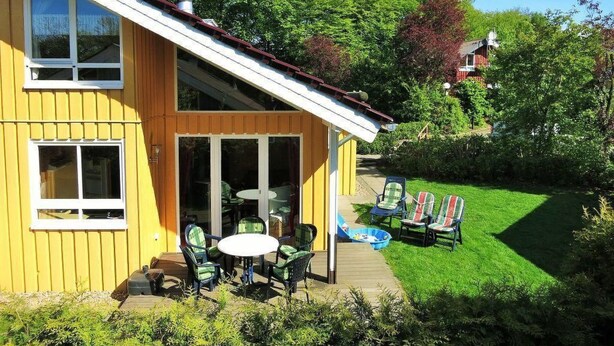 Ein gelbes Haus mit Schornstein, einer Terrasse mit Stühlen und Tisch sowie einem gepflegten Rasen.