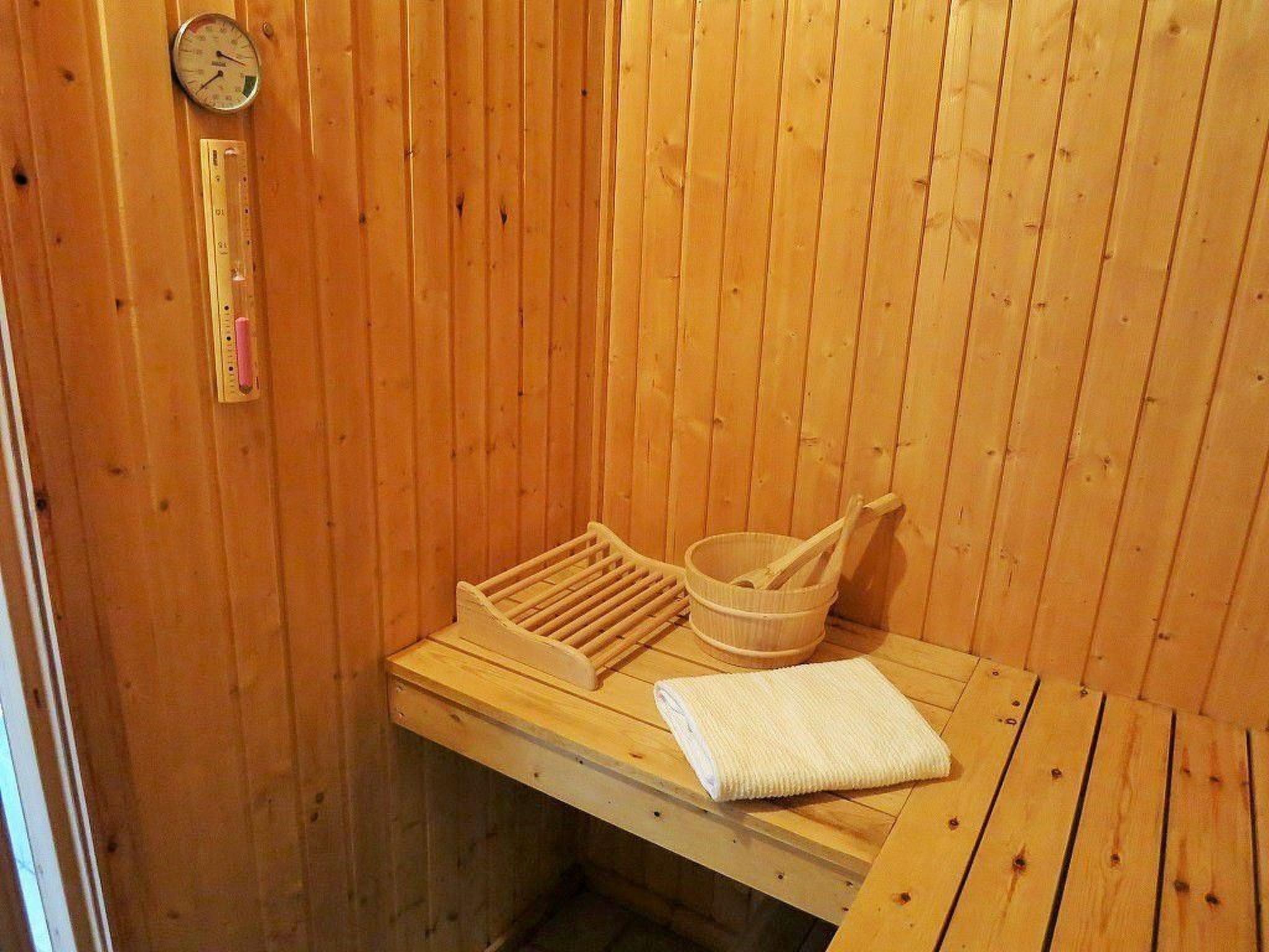 A wooden sauna with a bench, a wooden basin, and a towel.