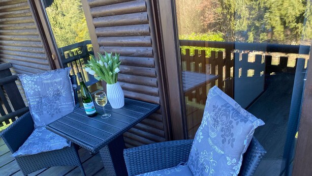 Eine Holzterrasse mit Korbmöbeln und einem Tisch, gedeckt mit einer Weinflasche und einem Glas.