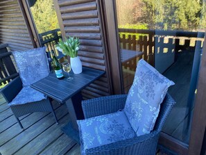 Una terraza de madera con mobiliario de mimbre y una mesa dispuesta con una botella de vino y una copa.