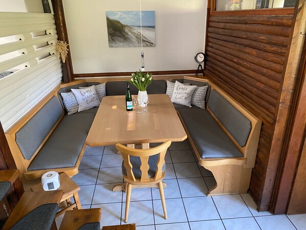Un coin salon accueillant avec une table en bois, des bancs rembourrés et une petite table sur laquelle se trouvent une bouteille et des verres.