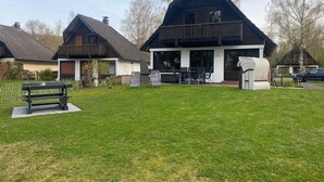 Ein zweistöckiges Haus mit Balkon, Rasen und einer Bank.