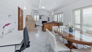 Eine moderne Küche mit Kochinsel, ein Essbereich mit Glastisch und ein Wohnbereich mit Sofa und Fernseher.
