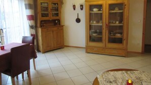Un comedor con una mesa y sillas de madera, un armario con puertas de vidrio y suelo de baldosas.