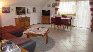 Una sala de estar acogedora con un sofá, una mesa de centro, un televisor y un comedor con sillas y una mesa.