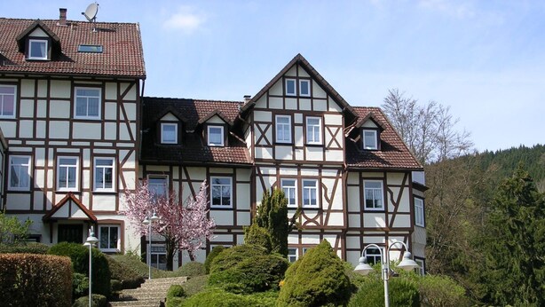 Ein großes, mehrgeschossiges Gebäude mit einer traditionellen Fachwerkausfachung, umgeben von gepflegten Gärten und blauem Himmel.