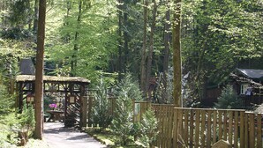 Ein bewaldetes Gebiet mit einer Holzhütte, einer Bank und einem Steinschild.