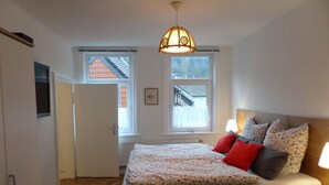 Ett sovrum med en säng, ett sängbord, en lampa och två fönster.