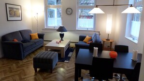 Ett modernt vardagsrum med en soffa, ett soffbord, en pall och en matplats med ett bord och stolar.