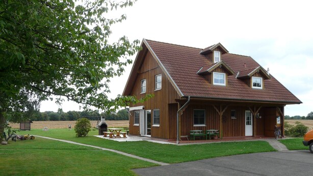 A wooden house with a sloped roof, a porch with benches, and a paved driveway. - für 16 Personen mit Terrasse by Interhome (Sudwalde)