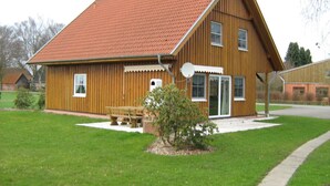 A wooden building with a sloped roof, a bench, and a small tree in the front yard. - für 16 Personen mit Terrasse by Interhome (Sudwalde)