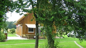 A wooden cabin with a covered porch, a lawn, and a car parked nearby. - für 16 Personen mit Terrasse by Interhome (Sudwalde)