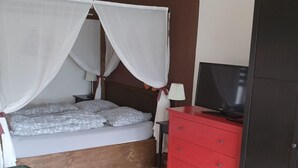 Una camera da letto con un letto a baldacchino, una cassettiera rossa, una televisione e una poltrona verde.