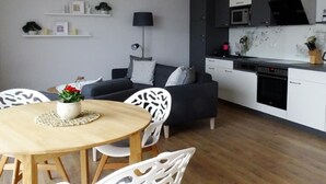 Una cocina moderna con gabinetes blancos, microondas y lavavajillas. Hay un comedor con una mesa redonda de madera y sillas blancas.