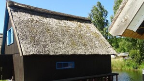 Una casa con techo de paja, una ventana pequeña y ubicada junto al agua.