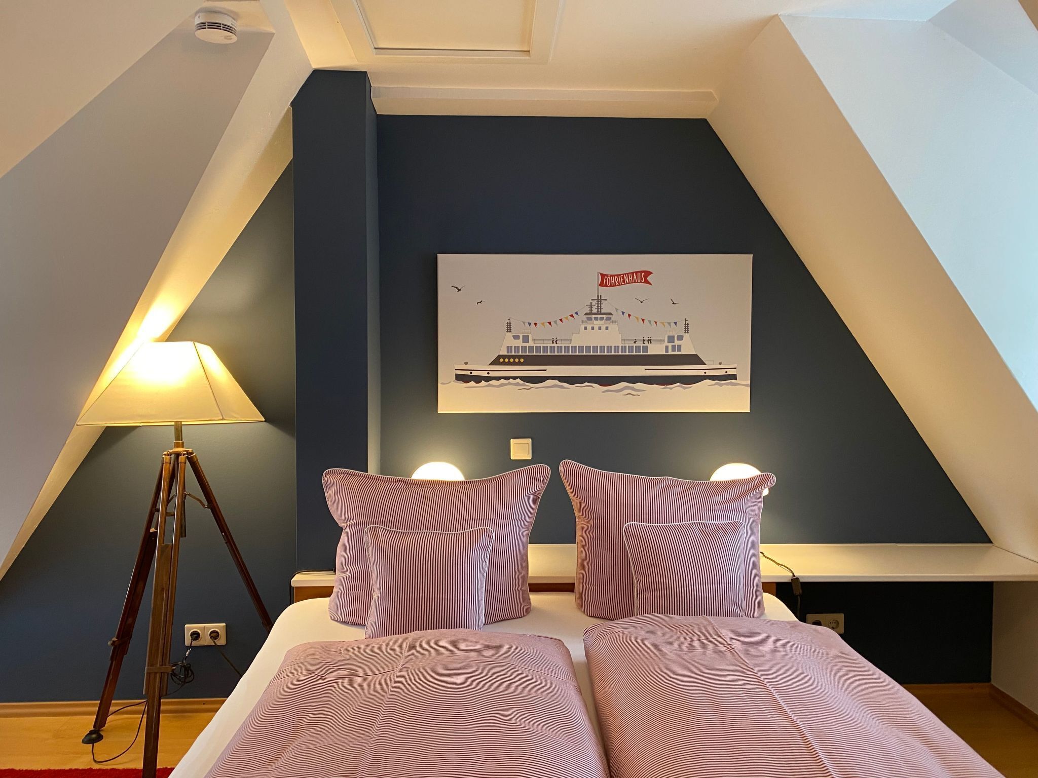 Camera da letto con un letto, due lampade da comodino, un quadro appeso al muro e una lampada da terra.