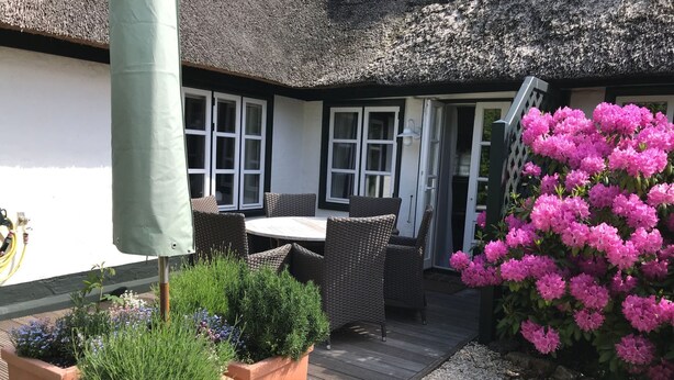 Een terras buiten met wicker meubels, een rieten dak en potplanten.