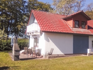 Une maison avec un toit rouge, un garage et une terrasse avec des chaises.