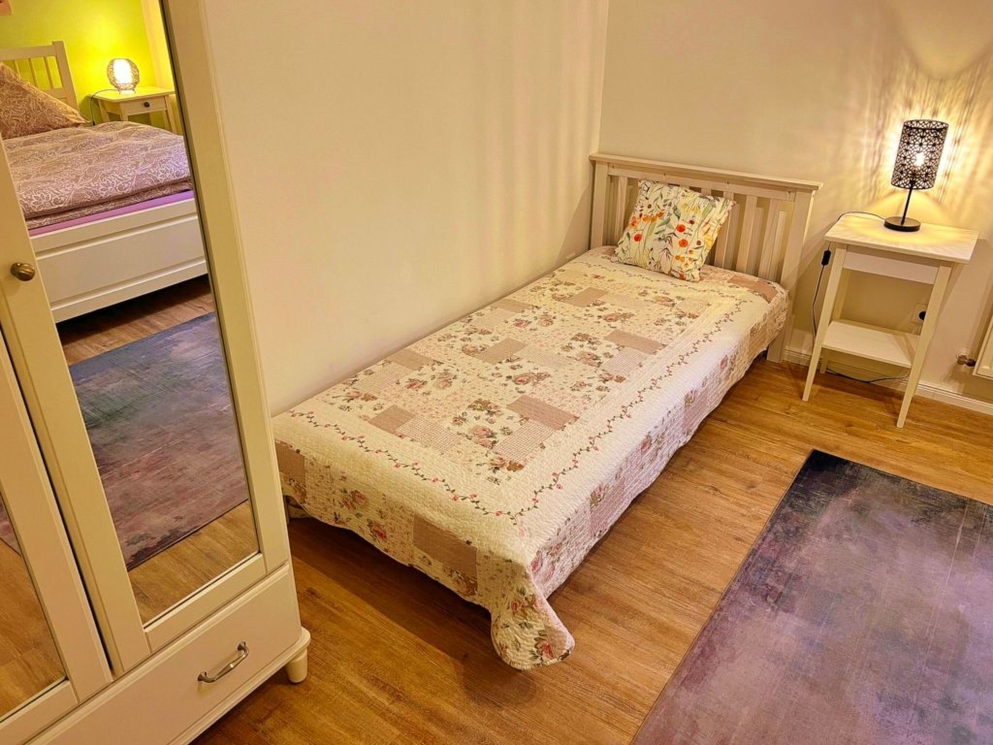 Een kleine, knusse slaapkamer met een enkel bed, een nachtkastje en een bijzettafeltje met een lamp.