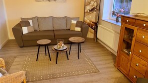 A living room with a sofa, two small tables, a wooden cabinet, and a window with a view. - Alles im grünen Bereich by Interhome (Bohmstedt)