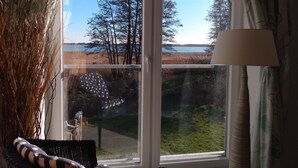 A room with a large window overlooking a lake and trees. There is a lamp on the right side of the window. - Admiral's Corner Luv by Interhome (Born)
