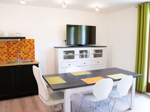 Eine moderne Küche mit schwarzem Arbeitsplatz, weißen Schränken und einem großen Flachbildfernseher, der über den Schränken angebracht ist.