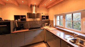 Een moderne keuken met houten balken, granieten aanrecht en een raam met uitzicht op groen.