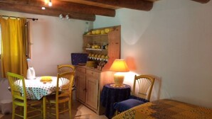 A cozy room with a dining table, two chairs, a bed with a patterned blanket, a small table with a lamp, and a shelf with kitchen items. - weg von der Zuvielisation by Interhome (Menzonio)