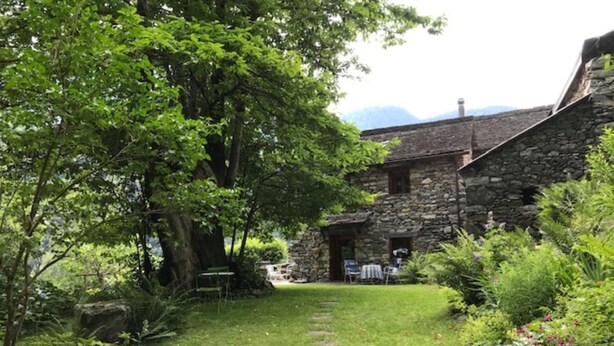 A stone building with a stone staircase leading to a door, surrounded by lush greenery and a well-maintained lawn. - weg von der Zuvielisation by Interhome (Menzonio)