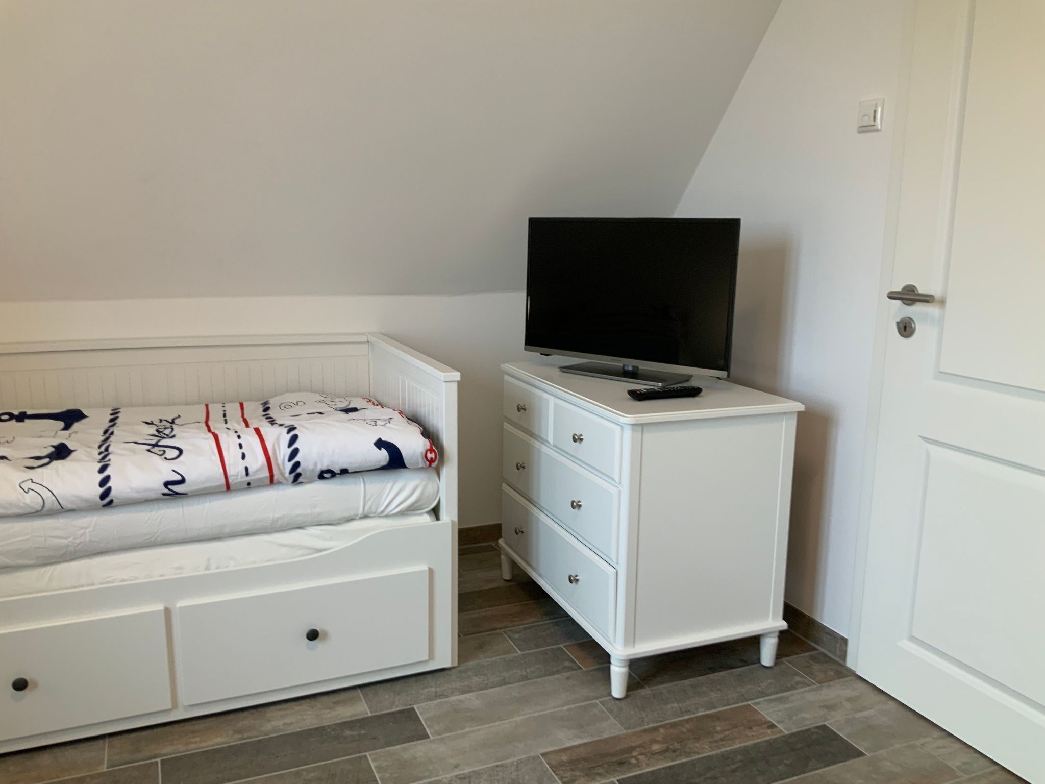 Une chambre à coucher avec un lit, une commode, un téléviseur et une porte.