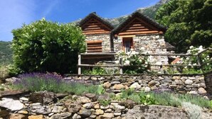 Un rustico chalet in pietra con tetto in legno, immerso nel verde e circondato da un muro in pietra.