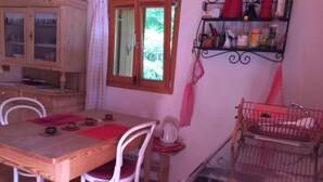 Zona pranzo con tavolo in legno, sedie bianche, tappetino rosso e angolo cottura con piano cottura e lavello.